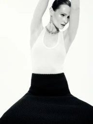 Model in white tank top and black skirt posing against white seamless background with arms raised