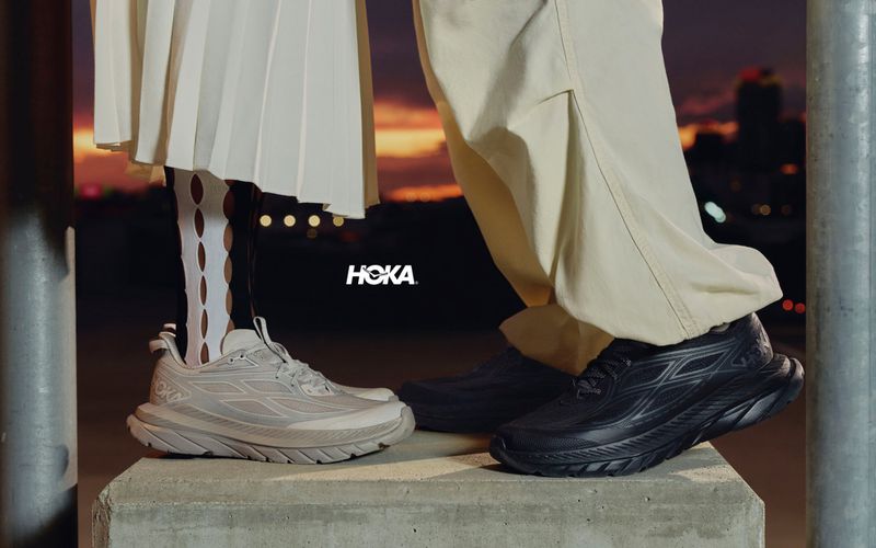 Close-up shot focusing on two people wearing Hoka running shoes standing on a concrete block outdoors at dusk.