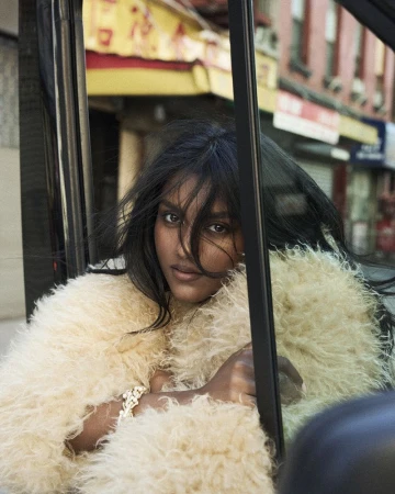 South Asian woman wearing a fluffy cream coat looking through a vehicle window