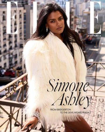 Simone Ashley wearing a fluffy white faux fur coat on a rooftop balcony with a city street visible below