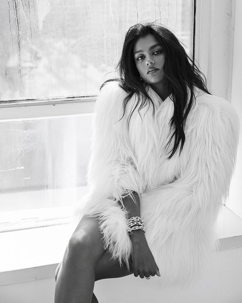 Monochrome fashion portrait of a woman wearing a fluffy white coat seated by a window.