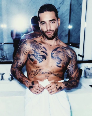 Portrait of Maluma with extensive upper body tattoos and a white towel wrapped around his waist in a bathroom