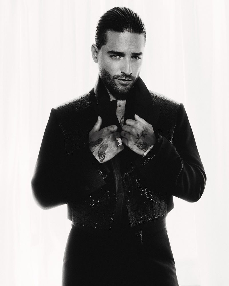 Portrait of Maluma wearing a dark embellished jacket against a bright white background
