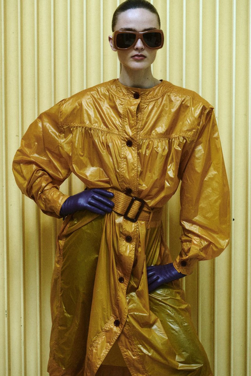 Model Gertrud Rose in an amber coat with dark sunglasses and purple gloves against a ribbed background for Re-Edition Magazine