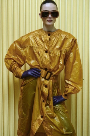 Model Gertrud Rose in an amber coat with dark sunglasses and purple gloves against a ribbed background for Re-Edition Magazine
