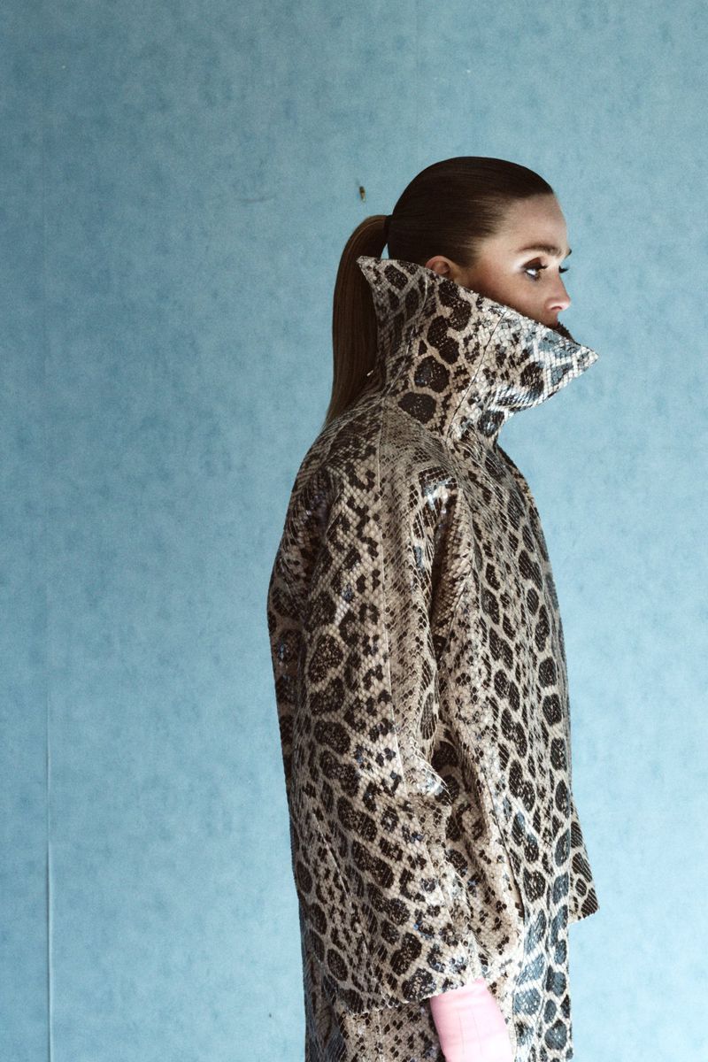 Model Gertrud Rose in an animal print coat with a high collar against a textured blue wall for Re-Edition Magazine