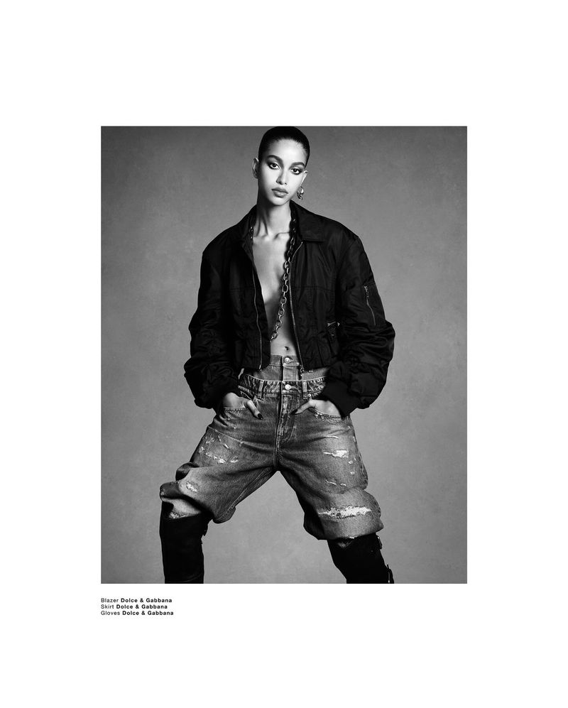 Model Luna Yohannan in a black bomber jacket and distressed denim jeans against a grey seamless background.