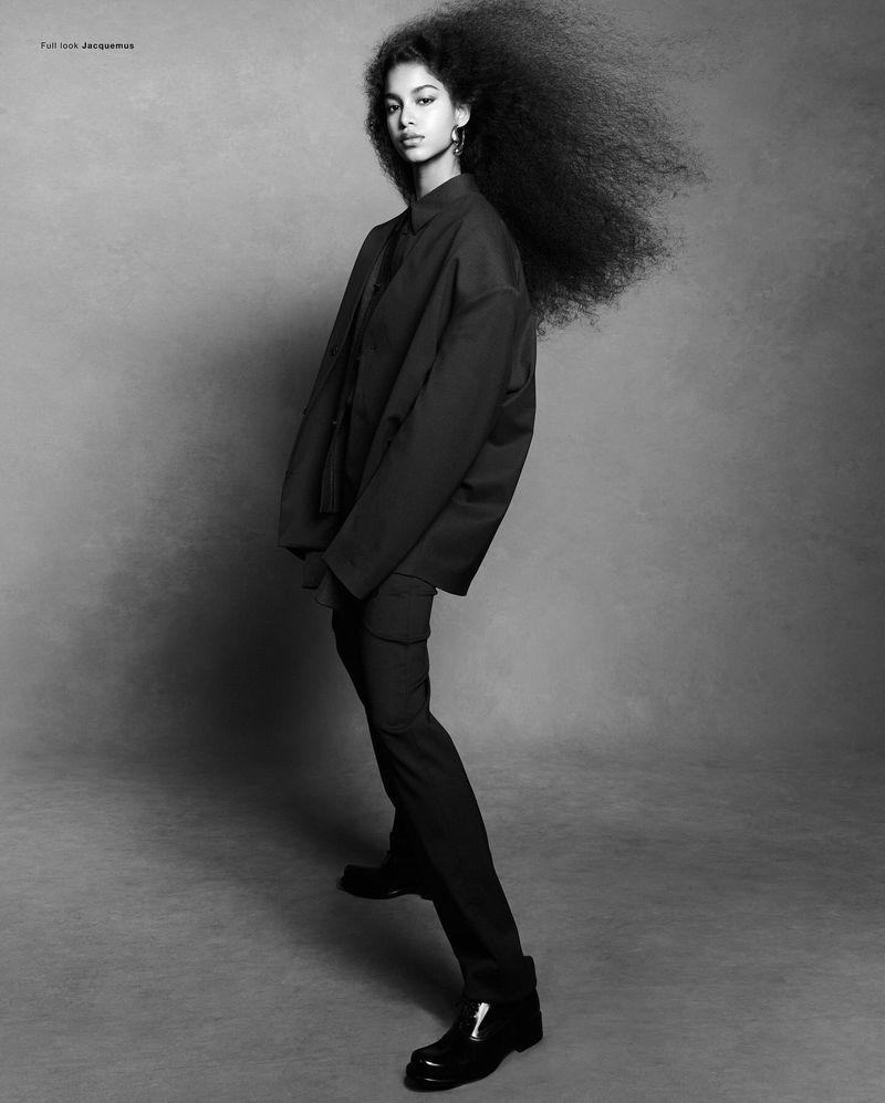 Model Luna Yohannan in dark attire with voluminous hair against a grey seamless background