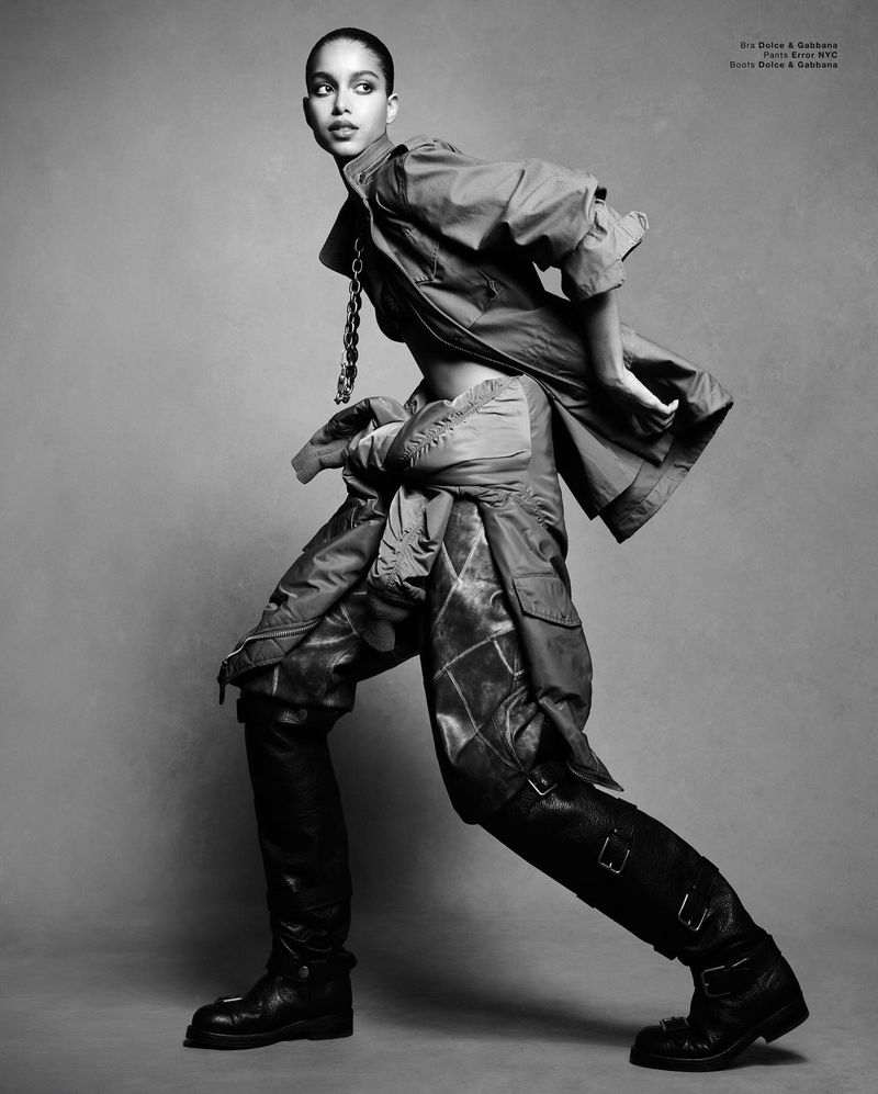 Model Luna Yohannan in layered utility outerwear and buckled boots against a textured grey background by Luigi & Iango