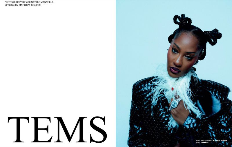 Portrait of singer Tems with styled hair buns wearing a black jacket and white feather collar against a blue background