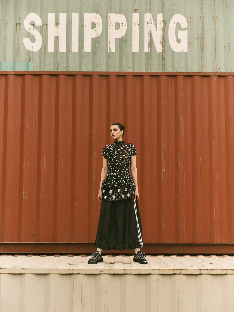 Model Nassia Matsa standing in front of large red and green shipping containers for Vogue Greece Adistar editorial