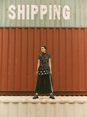 Model Nassia Matsa standing in front of large red and green shipping containers for Vogue Greece Adistar editorial