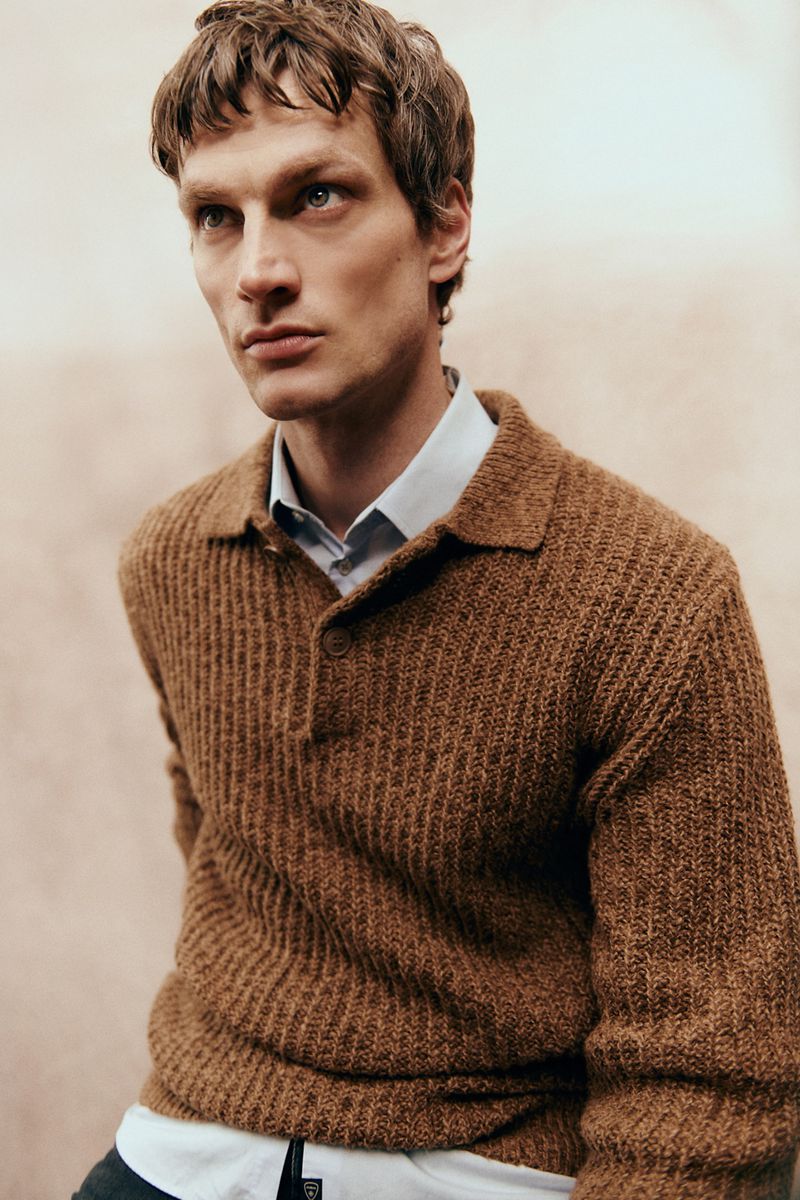 Close-up portrait of a male model wearing a brown ribbed knit polo shirt over a light collared shirt for Sicky Magazine.