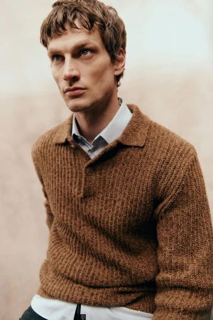 Close-up portrait of a male model wearing a brown ribbed knit polo shirt over a light collared shirt for Sicky Magazine.