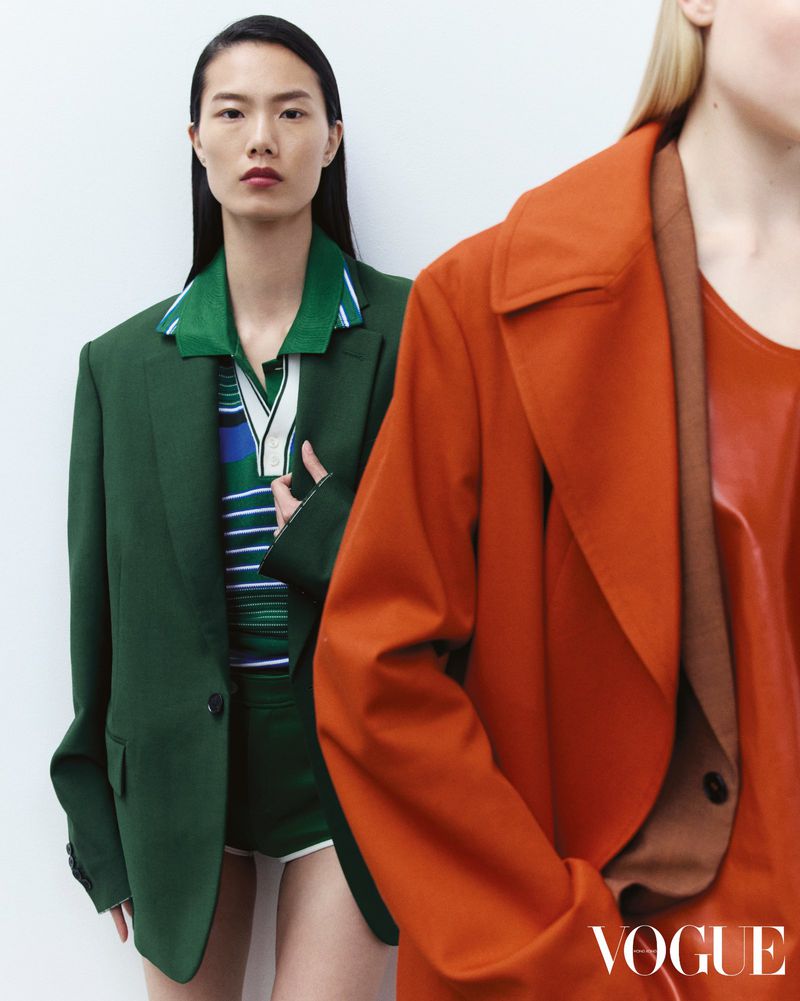 Two models wearing green and orange blazers against a plain white studio background for Vogue Hong Kong.