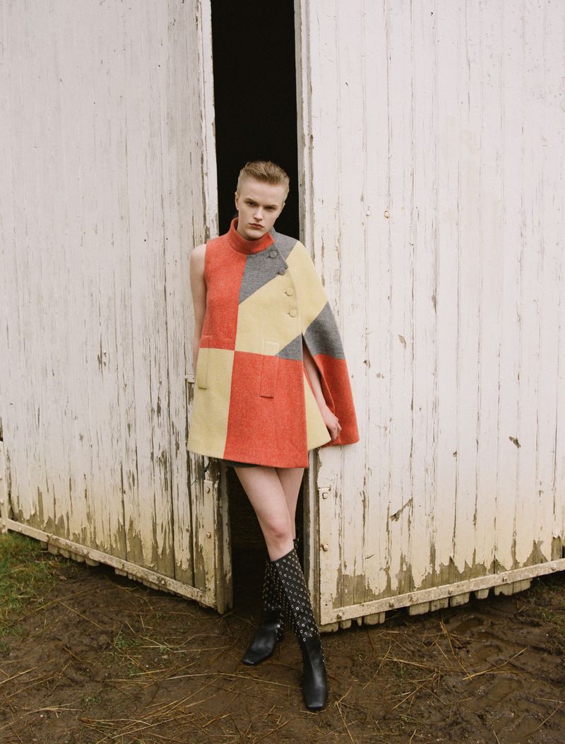 Model Hannah Motler wearing colour block cape standing in open barn doorway photographed by Giuseppe Triscari