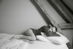 Model Hannah Motler lying on a bed under exposed wooden beams in a black and white editorial photograph.
