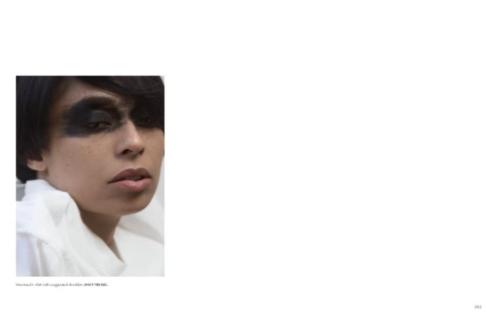 Close-up portrait of a model with heavy black eye makeup and a white collared shirt against a white background