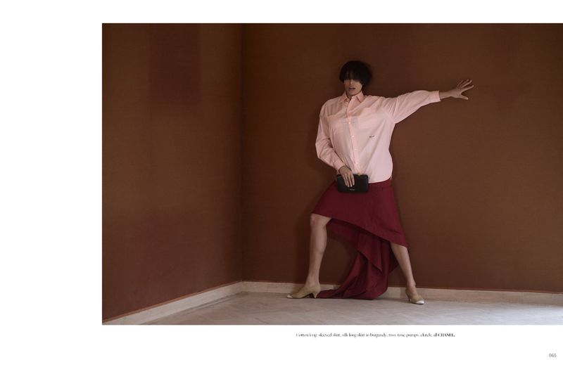 Model wearing a pink long-sleeved shirt and burgundy skirt leaning against a brown wall for Dry Clean Only Magazine