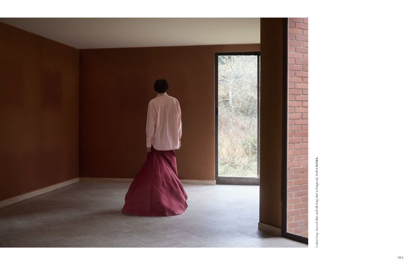 A person viewed from behind wearing a pink shirt and a long burgundy skirt in a room with terracotta-colored walls.