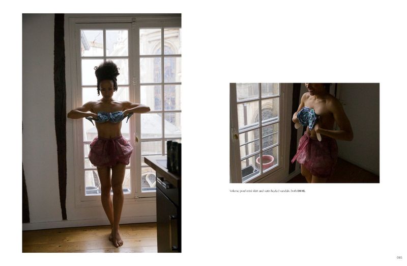 Model standing in front of French doors wearing a textured mini skirt and holding shoes against her chest