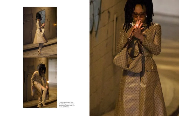 Model wearing a patterned coat and holding a shoulder bag while lighting a cigarette in an underpass