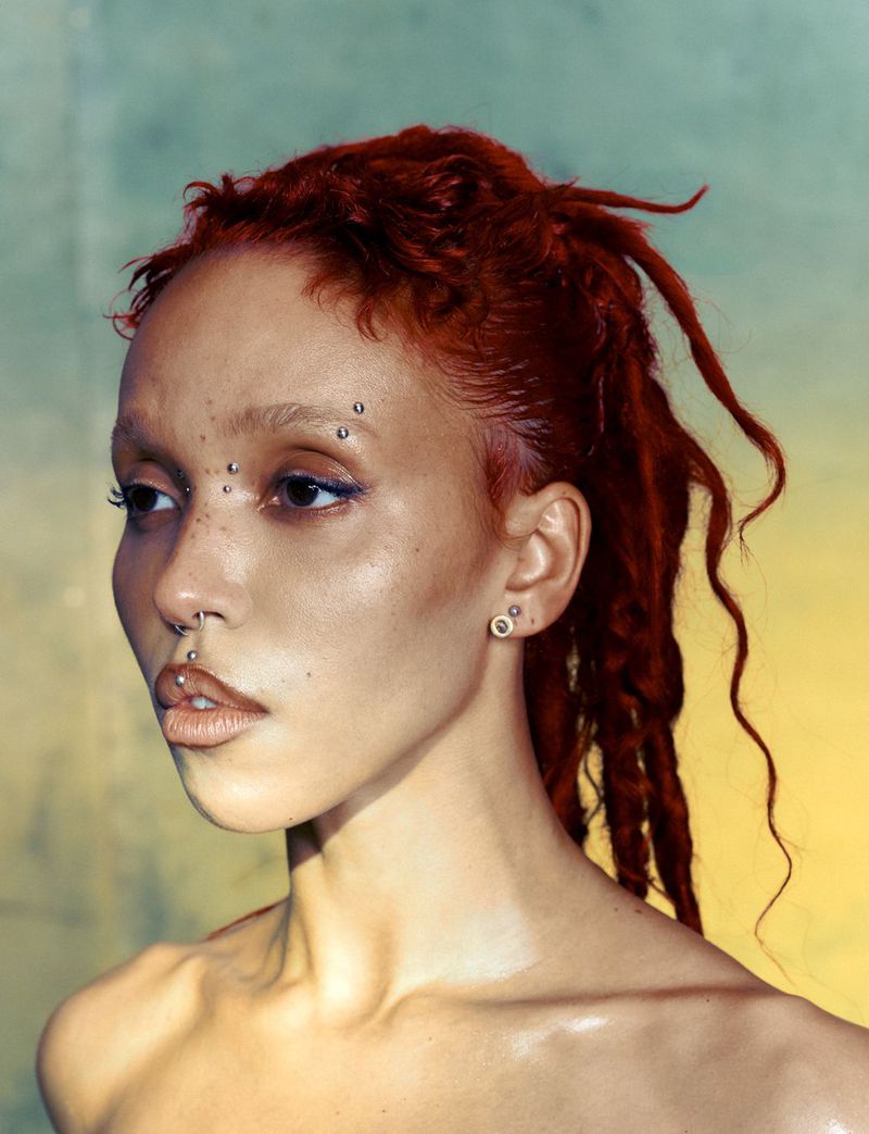 Portrait of FKA Twigs with red hair, facial piercings, and freckles against a gradient background for 10 Magazine