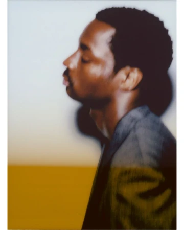 Profile portrait of a Black man with short dark hair wearing a grey jacket against a neutral studio background