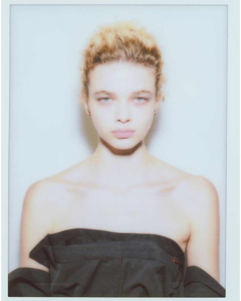 Portrait of a model wearing a black top against a plain white background presented in a polaroid frame.