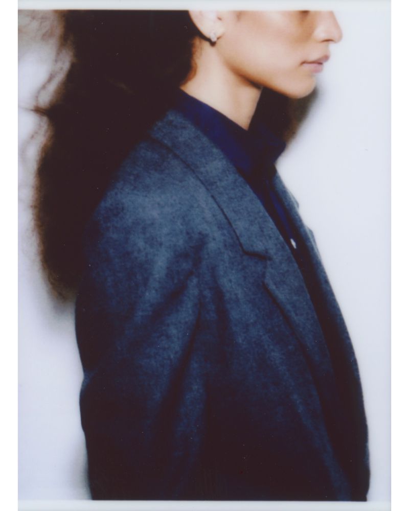 Profile portrait of a woman wearing a dark blazer over a dark top against a plain white wall