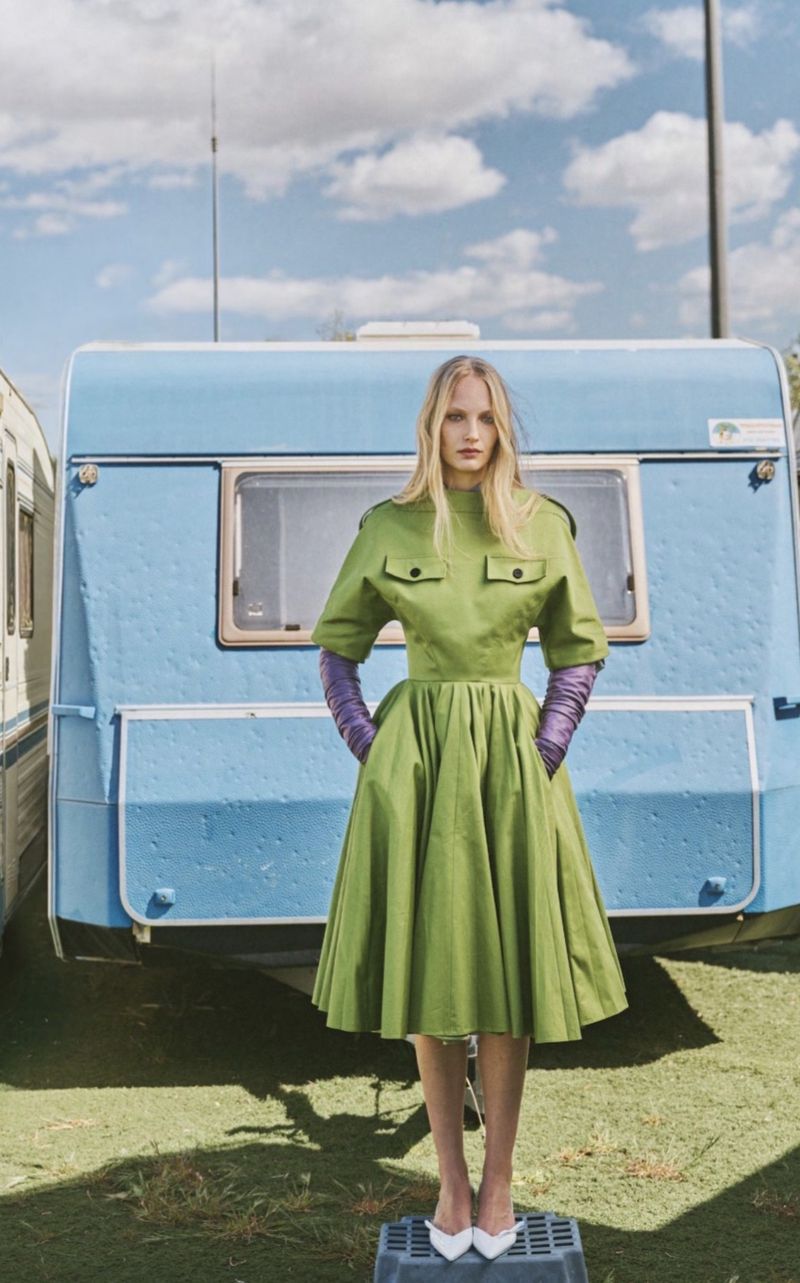 Model wearing green dress and purple gloves standing in front of a blue caravan for Elle Greece Road Trip