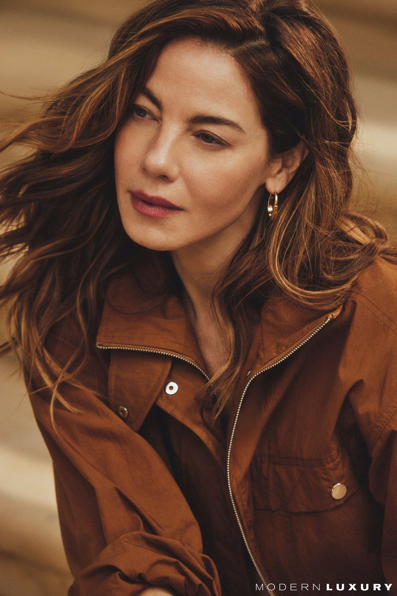 Michelle Monaghan wearing a brown jacket with gold hoop earrings in a portrait for Modern Luxury
