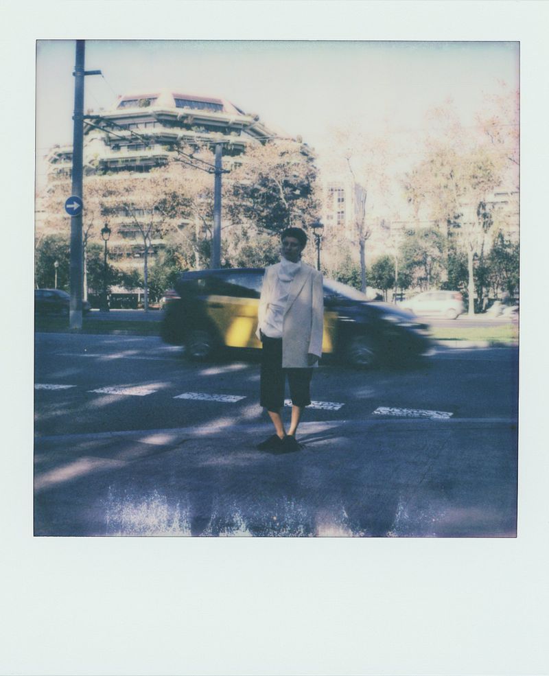 Man standing on a crosswalk in an urban scene with a taxi cab in the background, captured with a polaroid-style frame.
