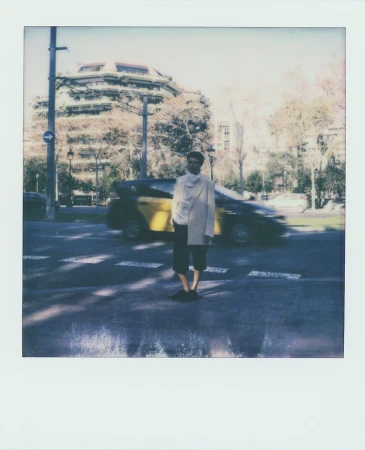 Man standing on a crosswalk in an urban scene with a taxi cab in the background, captured with a polaroid-style frame.