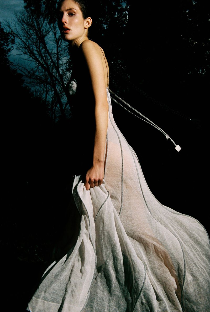 Model in a long sheer white gown outdoors against dark trees for The Collector Magazine editorial Stay Cool