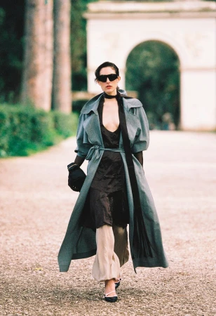 Model in sunglasses and a long grey coat walking on a park path for The Collector Magazine Stay Cool editorial
