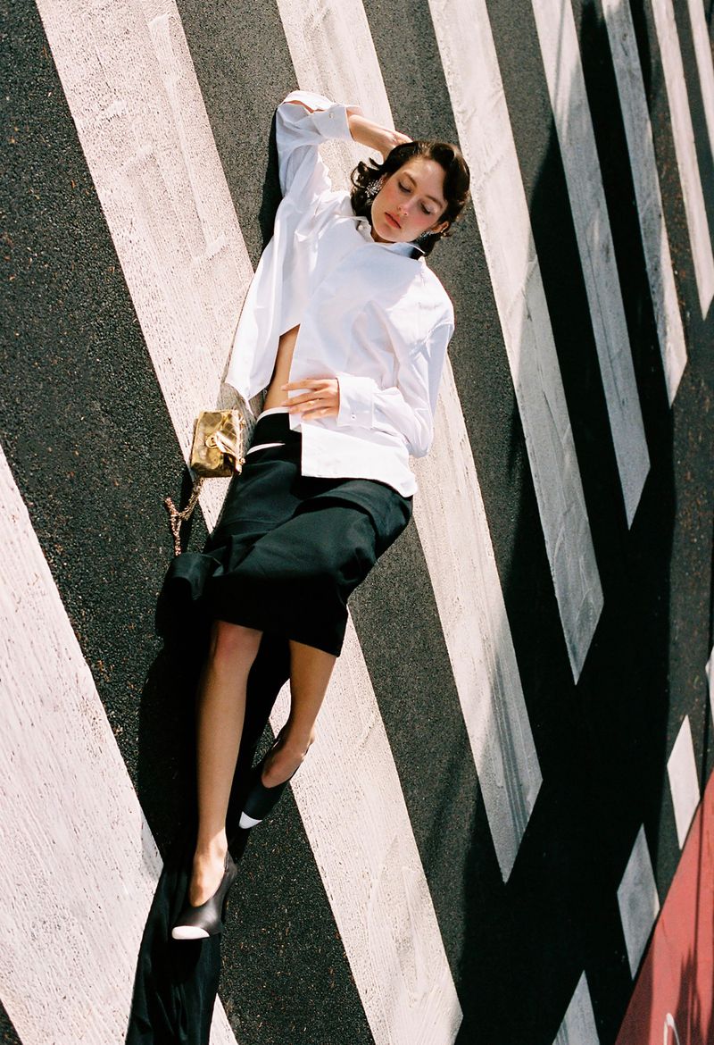 Model lying down on a striped crosswalk wearing a white button-down shirt and black skirt for The Collector Magazine
