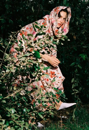 Model wearing a hooded floral dress partially hidden among garden foliage for The Collector Magazine Stay Cool project