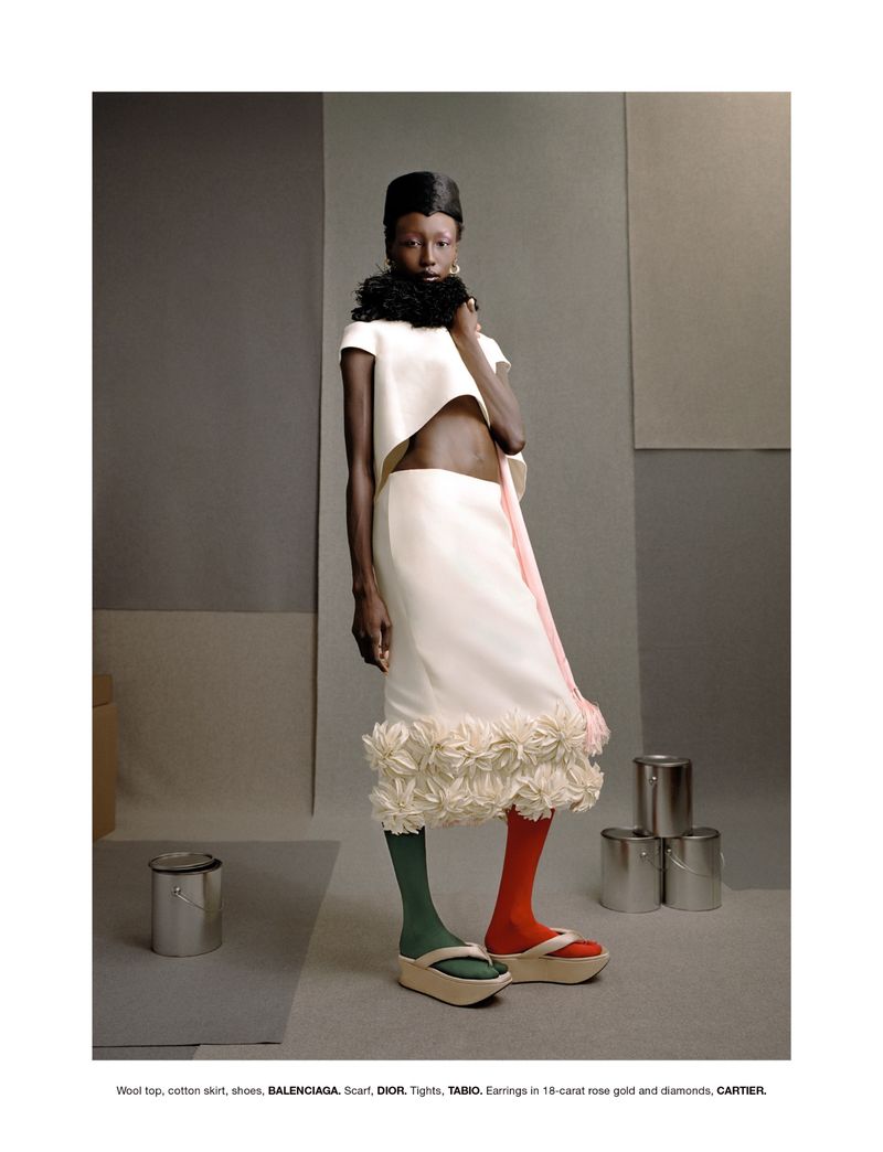 Model in white crop top and matching skirt with floral hem wearing green and red tights against a grey studio backdrop