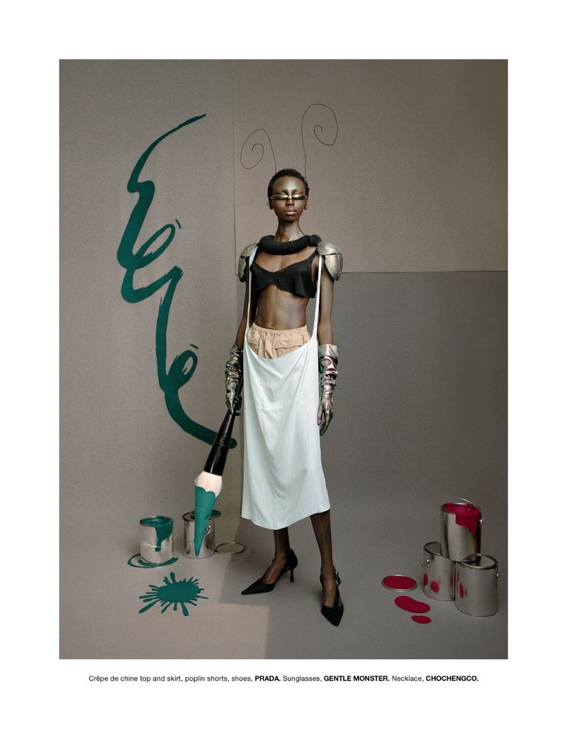Elegant editorial fashion photograph of a woman in a black top and a white skirt holding an oversized brush surrounded by colorful paint cans.