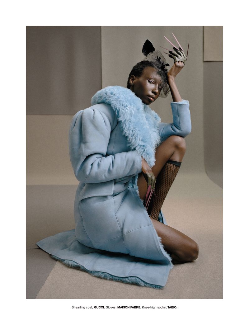 Model in light blue shearling coat and fishnet socks posing in front of a neutral studio backdrop for Numero New York.