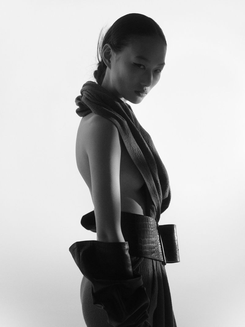 Model in silhouette wearing a dark wrapped top and wide belt against a bright white background