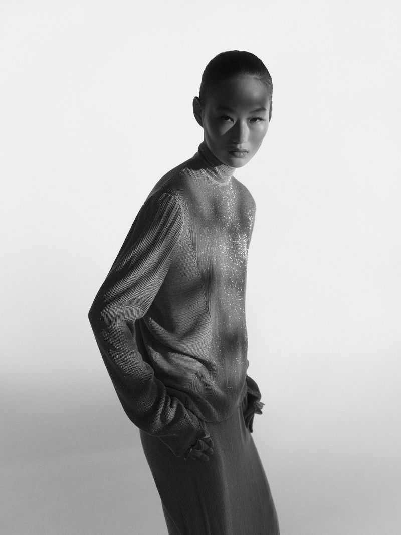 Model in textured turtleneck top and skirt against a bright white seamless background with dramatic shadow patterns across the face