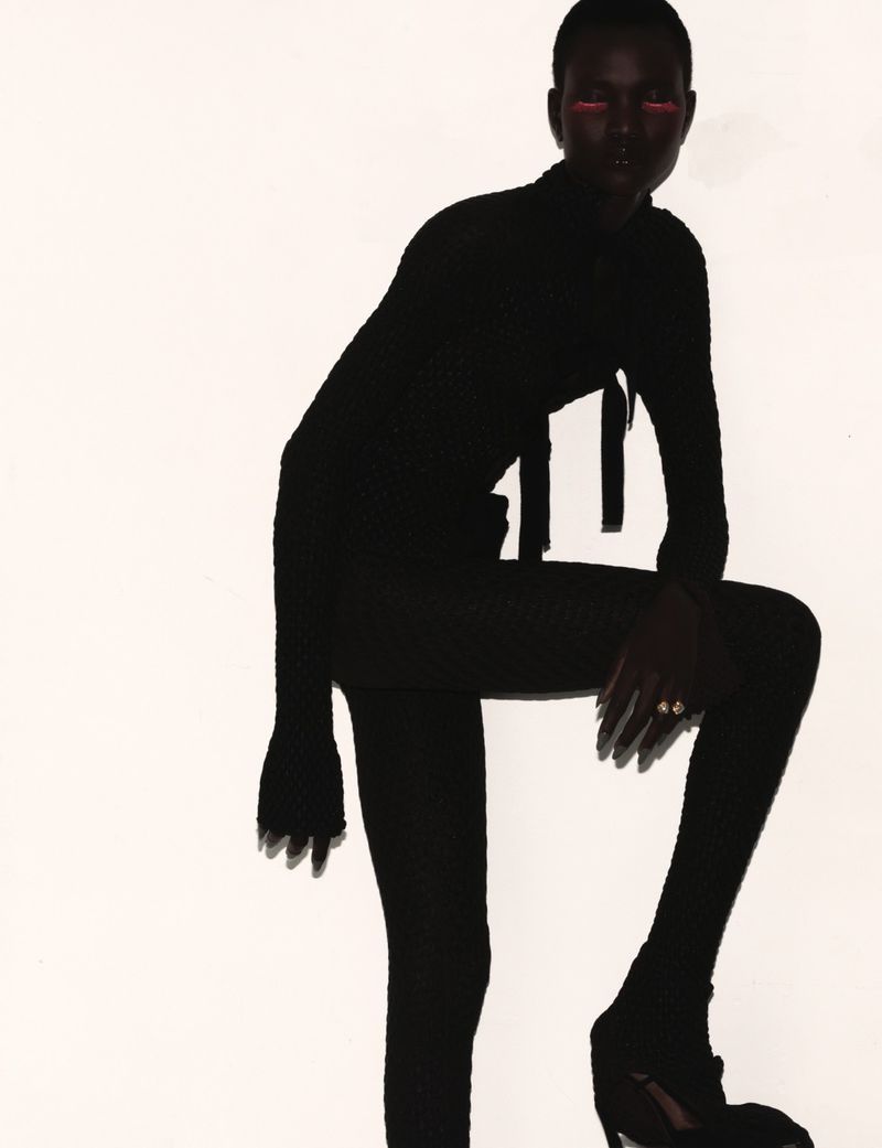 Model in dark silhouette wearing black clothing with vibrant red eye makeup against a bright white background