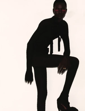 Model in dark silhouette wearing black clothing with vibrant red eye makeup against a bright white background
