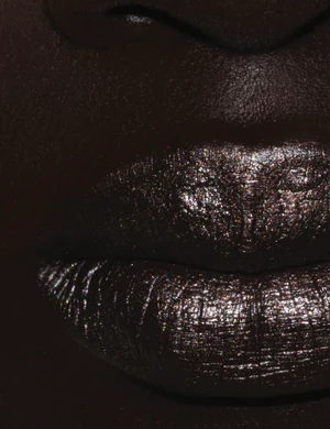Close-up macro shot of dark lips coated in metallic shimmer makeup with deep moody lighting for Dazed MENA.