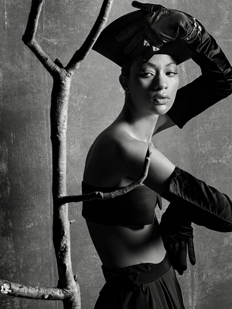 Monochrome fashion editorial portrait of model Selena Forrest wearing black opera gloves and a hat, posed near a bare tree branch