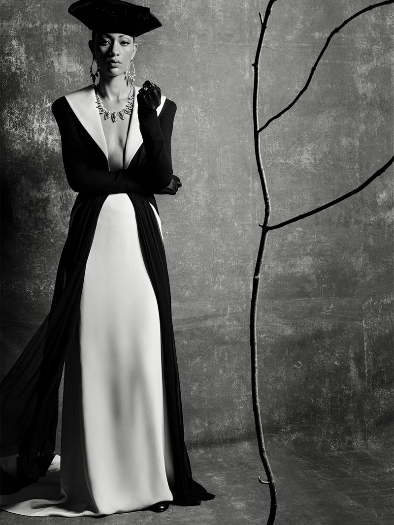 Model Selena Forrest in a black and white gown with a sculptural hat and statement jewelry against a textured backdrop