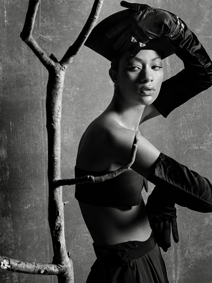 Monochrome fashion editorial portrait of model Selena Forrest wearing black opera gloves and a hat, posed near a bare tree branch