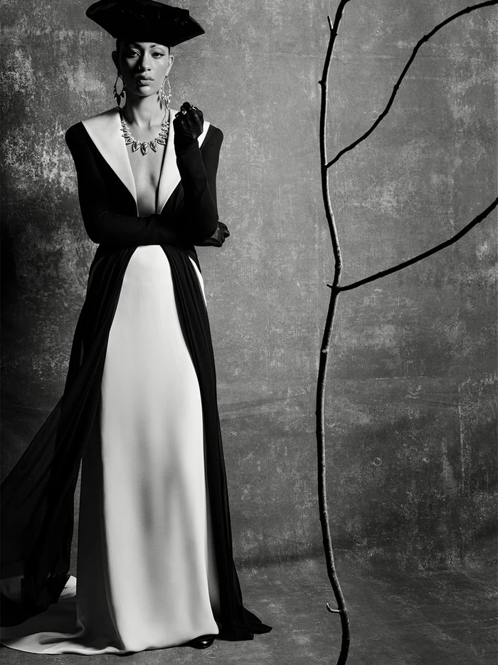 Model Selena Forrest in a black and white gown with a sculptural hat and statement jewelry against a textured backdrop
